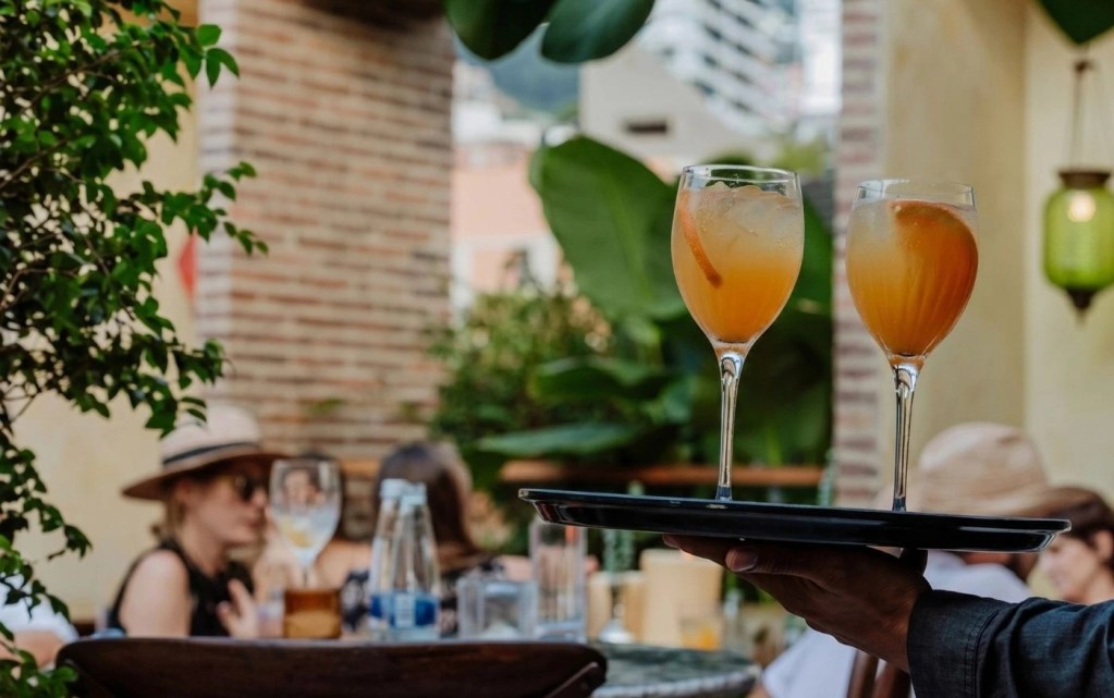 Mesero sirviendo dos cócteles cítricos en la terraza de El Zarzo Bar en Provenza, Medellín, beneficio exclusivo de reserva directa
