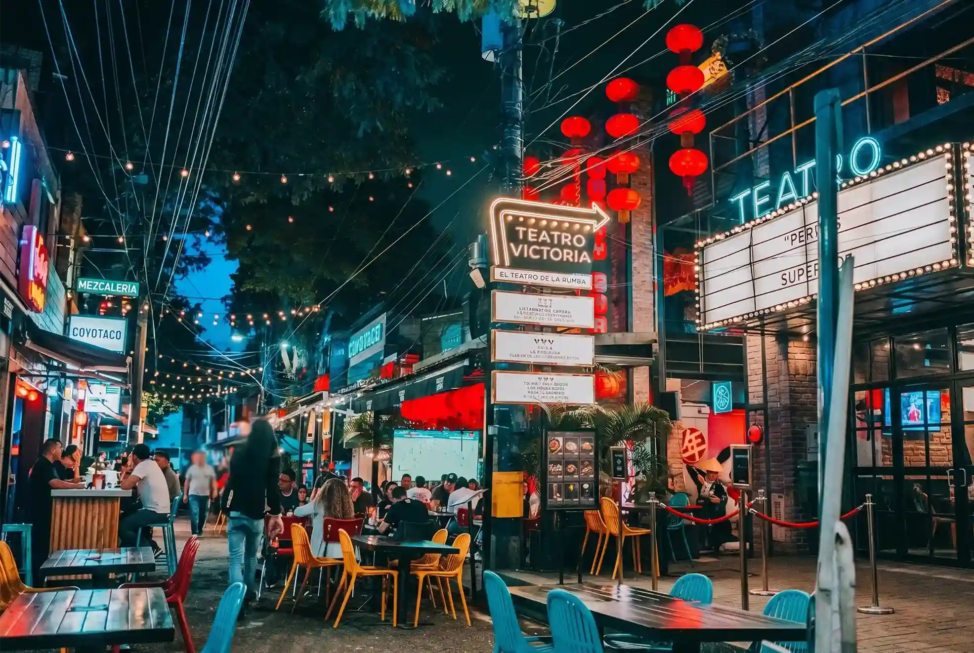 Calle de Provenza de noche con bares, neones y Teatro Victoria, barrio de Hotel El Zarzo en Medellín.