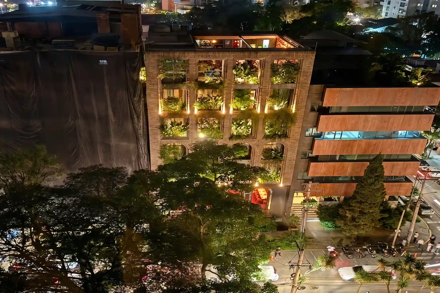 Hotel El Zarzo facade at night with lit vertical gardens and active street in Provenza Medellín.